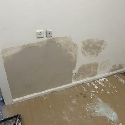 קיר עם תיקוני טיח וכתמי צבע על הרצפה