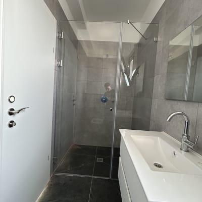 מקלחון זכוכית עם אריחים אפורים וברז מתכת