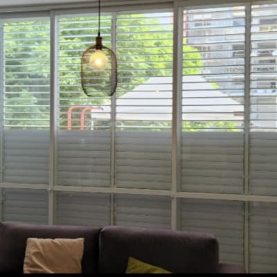 תריסים לבנים על חלון גדול עם נוף ירוק