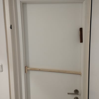 דלת לבנה עם ידית מתכת ומוט עץ לרוחב