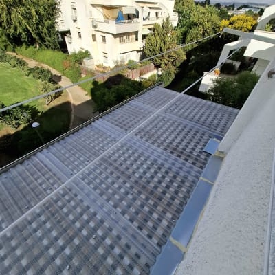 גג פלסטיק שקוף מותקן על מבנה ליד גינה