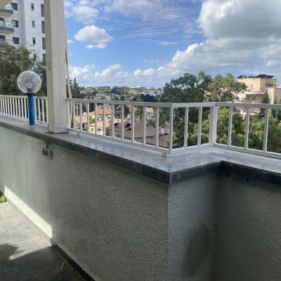 מעקה מרפסת עם נוף לעצים ובניינים ברקע