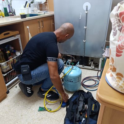 טכנאי מקררים עובד עם בלון גז וכלים ליד מקרר פתוח