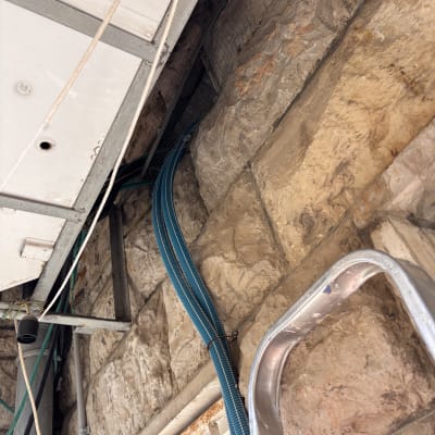 צינורות כחולים ליד קיר אבן עם סולם מתכת
