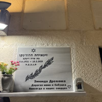 מצבה עם כיתוב בעברית ורוסית, פרחים ונר זיכרון