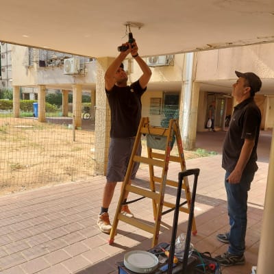 שני אנשים עובדים על תקרה עם כלי עבודה וסולם