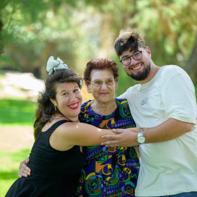 שלושה אנשים מחייכים מחובקים בפארק ירוק