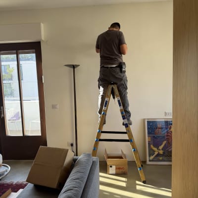 אדם על סולם מבצע עבודה חשמלית בקיר