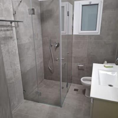 מקלחון זכוכית עם ראש מקלחת עגול וקירות אפורים