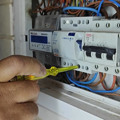 יד מחזיקה מברג ליד לוח חשמל עם חוטים