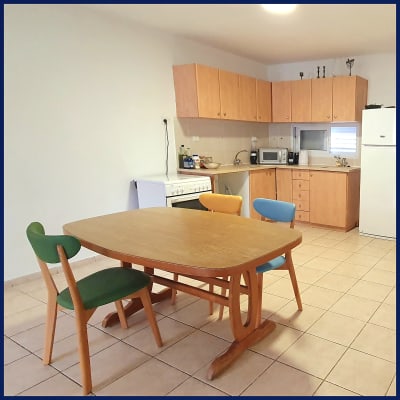 מטבח עם שולחן עץ וכיסאות צבעוניים, ארונות עץ ומכשירי חשמל.