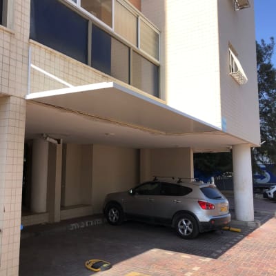 סוכך לבן מעל חניה עם רכב אפור