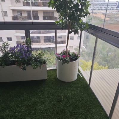 עציצים עם פרחים במרפסת עם דשא סינתטי