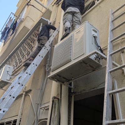 עובדים על סולם ליד מזגן מותקן על קיר חיצוני