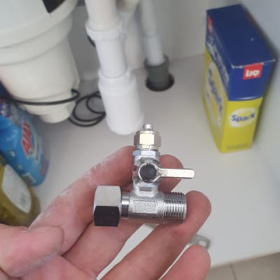 שסתום מתכת מוחזק ביד ליד צנרת מתחת לכיור