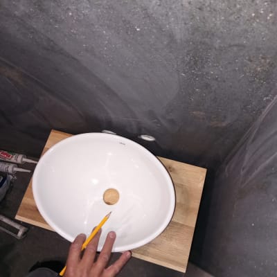 כיור עגול על משטח עץ, יד מחזיקה עיפרון