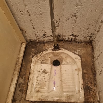 אסלה מזרחית עם צינור מים על קיר בטון