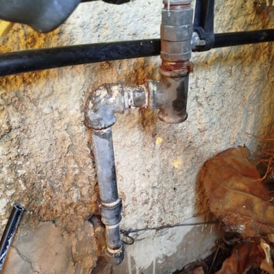 צנרת מתכת חלודה עם ברז ליד קיר