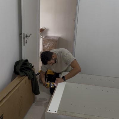 אדם מרכיב רהיט עם מברגה בחדר