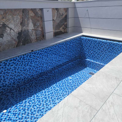 בריכה ריקה עם אריחים כחולים, קיר אבן וברז מים