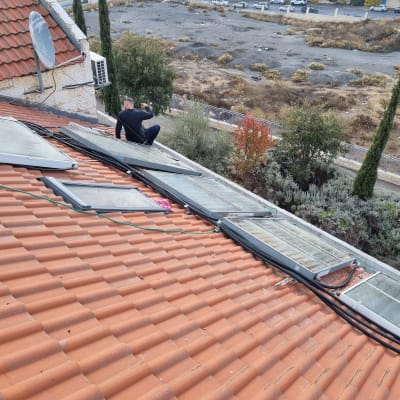 אדם יושב על גג רעפים ליד קולטי שמש