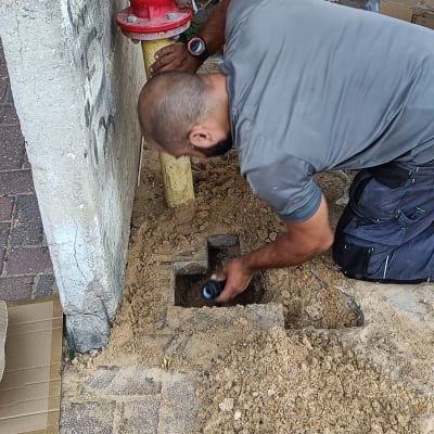 אדם עובד על צינור ליד ברז כיבוי אדום