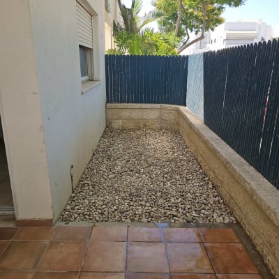 חצר עם אבנים, גדר עץ ועצים ברקע