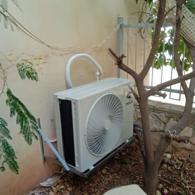 יחידת מיזוג אוויר מותקנת בחוץ ליד קיר ועצים