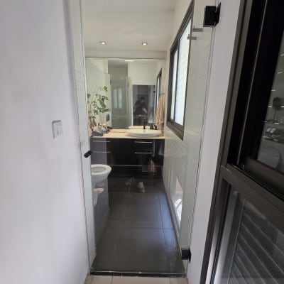 דלת זכוכית שקופה עם צירים וידית שחורים בכניסה לחדר רחצה