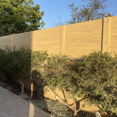 גדר עץ גבוהה עם שיחים ירוקים לפניה