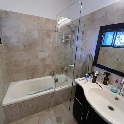 מקלחת עם דלת זכוכית, בקבוקי שמפו וסבון על המדף