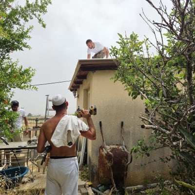 אדם מחזיק מקדחה ליד גג עם צמחייה מסביב