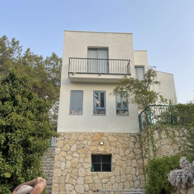 בית עם קירות אבן, מרפסת וחלונות כחולים.