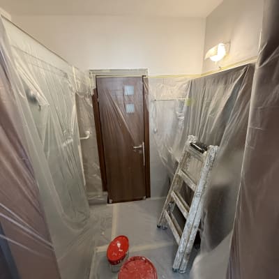 סולם ודליים בחדר מוכן לצביעה עם כיסויים פלסטיים.