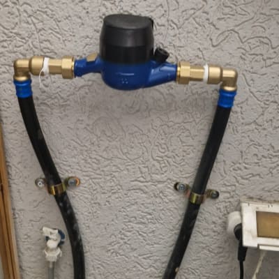 מד מים כחול עם צינורות מחוברים לקיר