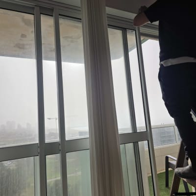 אדם מתקין תריסים ליד חלון גדול