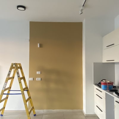 קיר צבוע בצבע חום, סולם צהוב ודלי צבע