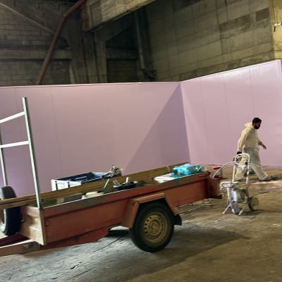 אדם בחליפת מגן צובע קיר סגול במחסן