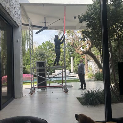 אדם על סולם מתקין מאוורר תקרה בחוץ