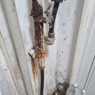 צינור חלוד עם נזילה על קיר לבן