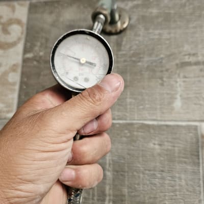 מד לחץ מים מוחזק ביד על רקע רצפה