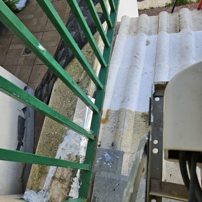 חומר איטום לבן על גג רעפים ליד מעקה ירוק