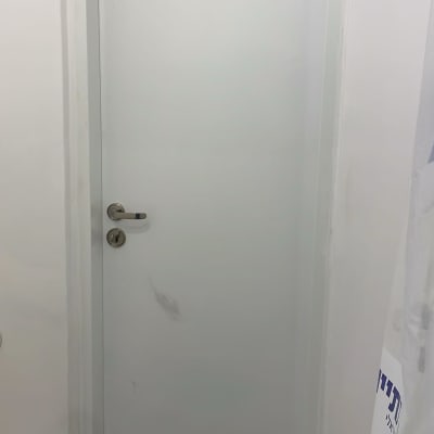 דלת לבנה עם ידית מתכת על רקע קיר לבן