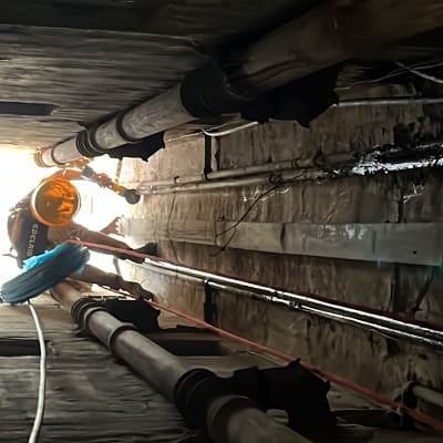 אדם עם קסדה עובד בצינורות במנהרה צרה