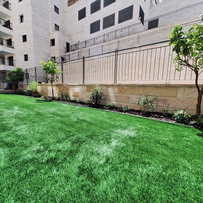 דשא ירוק עם עצים ופרחים ליד בניין מגורים