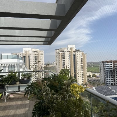 מרפסת עם צמחייה ורשת הגנה על רקע בניינים