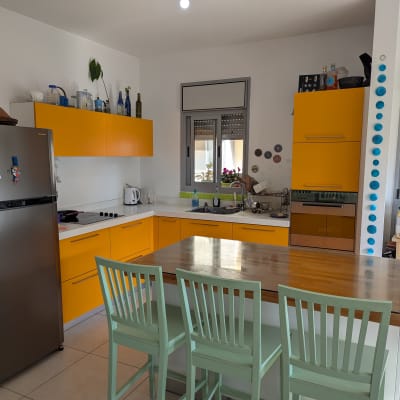 מטבח עם ארונות צהובים, מקרר נירוסטה וכיסאות ירוקים
