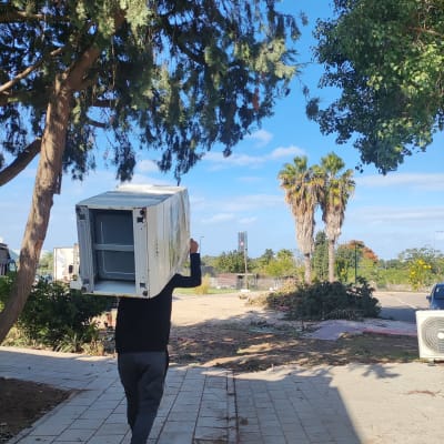 אדם נושא מקרר על כתפיו בשביל מרוצף