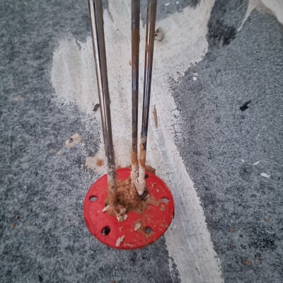 תקריב של מוטות מתכת בבסיס אדום על משטח בטון