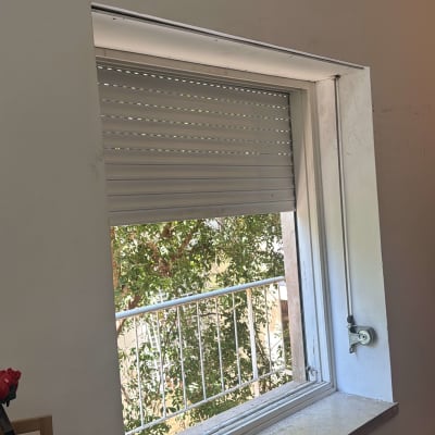 חלון עם תריס גלילה פתוח חלקית ונוף עצים בחוץ